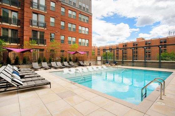 Luxurious apartment complex featuring a sparkling outdoor pool, modern lounge chairs, and vibrant umbrellas against a backdrop of stylish brick buildings.