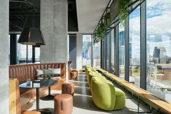 Modern urban lounge with plush green seating, sleek leather booths, and panoramic city views through floor-to-ceiling windows.