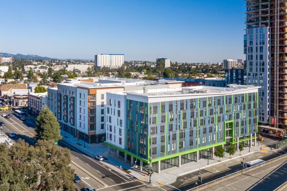 Modern multi-story urban apartment complex with sleek design, broad windows, and vibrant green accents, situated in a bustling city area.