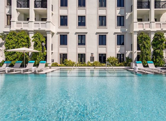 Luxurious apartment complex featuring an inviting swimming pool surrounded by elegant lounge chairs and lush greenery.
