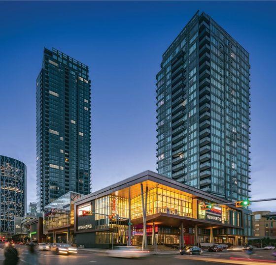 Modern high-rise apartment buildings with a vibrant commercial plaza at dusk, featuring sleek glass architecture and bustling city life.