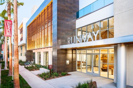 Modern apartment building exterior with sleek design and inviting entrance, surrounded by palm trees and vibrant landscaping.