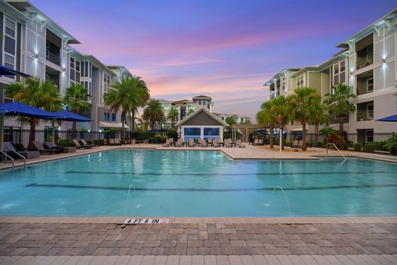 Luxurious apartment community at sunset with a sparkling swimming pool, surrounded by elegant modern architecture and lush palm trees.