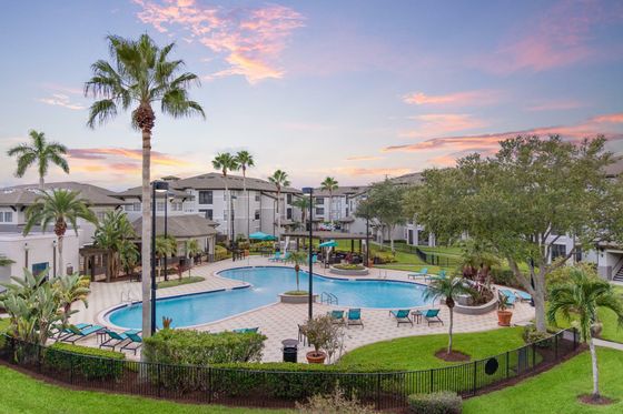Inviting community pool area surrounded by palm trees and modern apartments, with a backdrop of a stunning sunset sky.