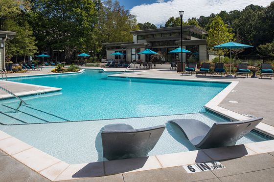 Luxurious outdoor pool area with stylish loungers and umbrellas, surrounded by lush greenery for a relaxing retreat.