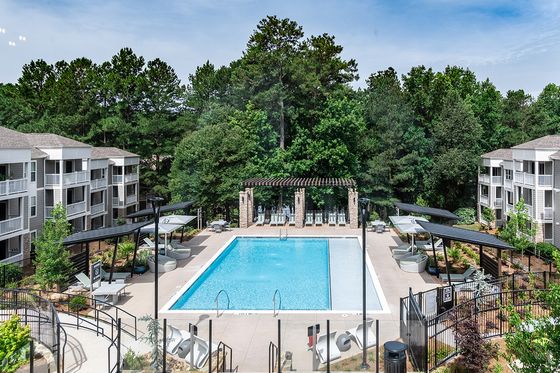 Luxurious apartment complex showcasing a sparkling pool with elegant lounge areas, surrounded by lush greenery and modern architecture.