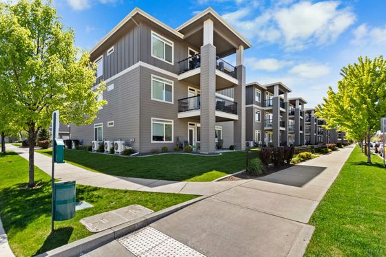 Modern three-story apartment building with balconies, surrounded by lush greenery and well-maintained pathways.