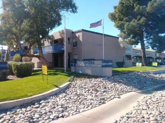 La Cima monument sign leading to the entrance. River rock and green grass landscaping with American flag. Blue balcony fencing