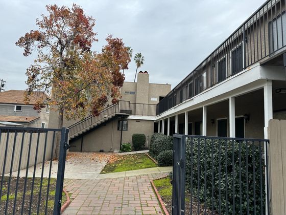 view of entrance to gate with black railing, a brick pathway leading inward, and grey exteriors with white trim on the building