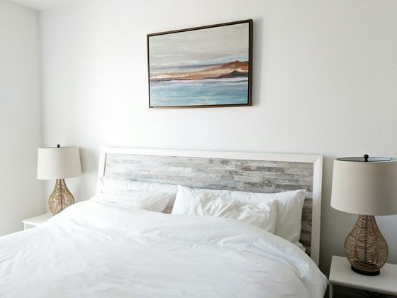 Light and airy bedroom with white sheets, two wicker lamps and painting on wall