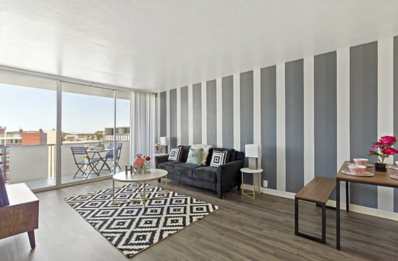stripes painted on back living room wall, view into patio with black couch and colorful rug in living room
