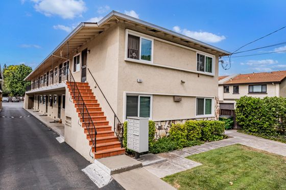 blue skies and green landscaping surrounding apartment building with staircase leading up to exterior upper level.