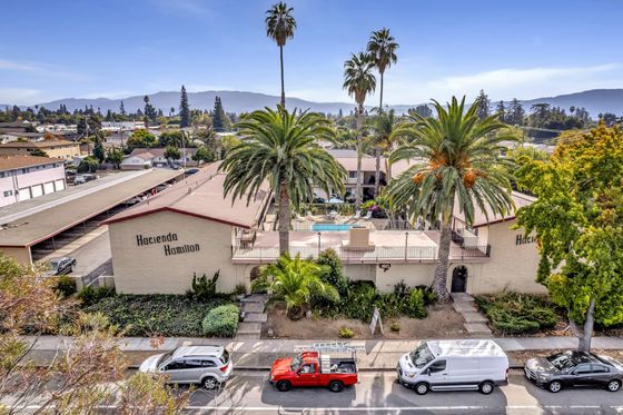 An aerial view of the Hacienda Hamilton apartment complex. The complex has a swimming pool, palm trees, and a parking lot