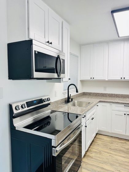 Open living space with a wall seperating the kitchen. Ceiling fan, white cabinets and white appliances featured in the kitchen