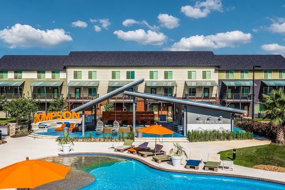 Vibrant apartment complex featuring a modern pool area with colorful lounge chairs and sunshades, perfect for relaxation and social gatherings.
