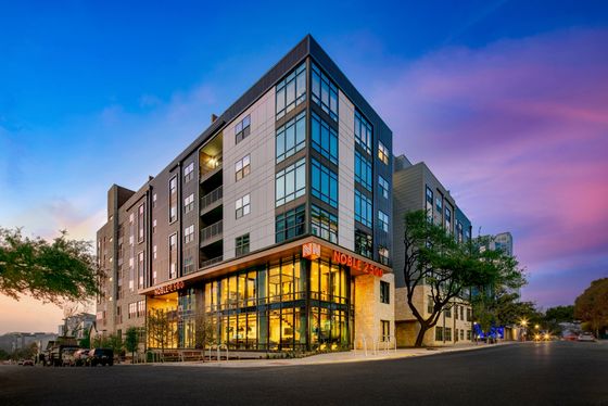 Modern apartment building with large windows at sunset, showcasing vibrant street-level lighting and a stylish urban design.