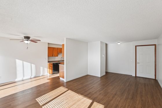 Bright and open living space with elegant wood flooring, modern ceiling fan, and a cozy kitchen featuring warm wooden cabinetry.