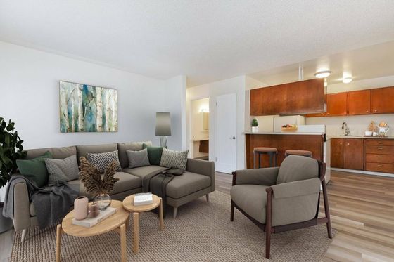 Inviting open-plan living room with stylish furniture, cozy sofa, modern armchair, and elegant decor, seamlessly connected to a sleek kitchen area.
