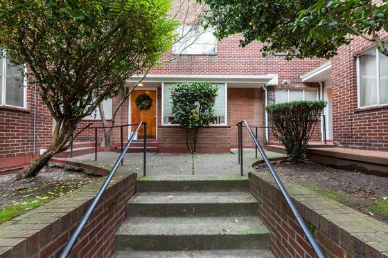 Inviting entrance to a cozy apartment, highlighted by vibrant greenery, brick facade, and elegant stairs with decorative railings.