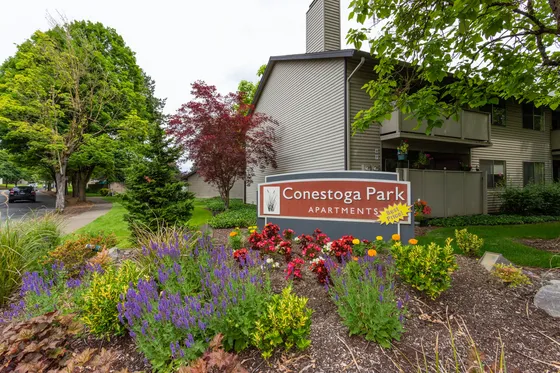 Charming Conestoga Park Apartments entrance surrounded by vibrant gardens and lush greenery, showcasing welcoming community living.