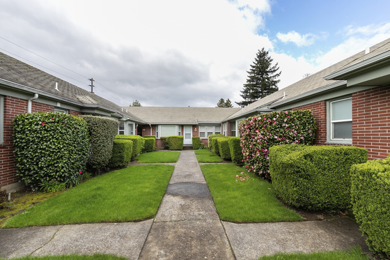 Charming courtyard view of a brick apartment complex with lush greenery and vibrant flower bushes.
