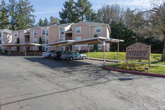Charming Kinnaman Terrace Apartments surrounded by lush greenery and offering ample parking spaces, set against a backdrop of beautiful trees.