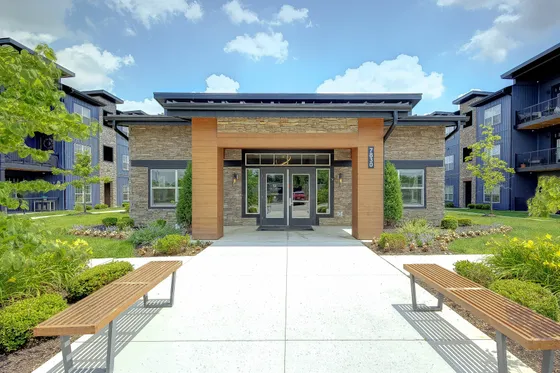 Elegant apartment complex entrance featuring modern architecture, lush landscaping, and inviting benches.