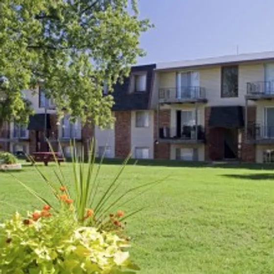 Exterior view of Rosewood Village Apartments in Springfield, Missouri, featuring a large green lawn, mature trees, and a two-story brick and siding building with private balconies.
