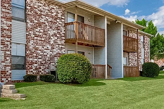 Exterior of Grandview Village Apartments on the north side of Springfield, MO, showing a two-story brick and siding building with exterior staircases, set against a bright blue sky and surrounded by well-maintained green lawn.