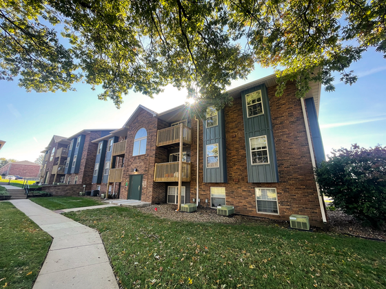 Charming brick apartment building with balconies, nestled among lush greenery and picturesque landscaping.