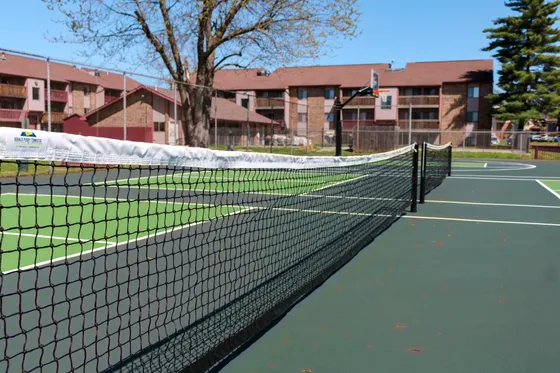 Inviting outdoor tennis court with vibrant green surface, surrounded by charming apartments and lush greenery, perfect for an active lifestyle.