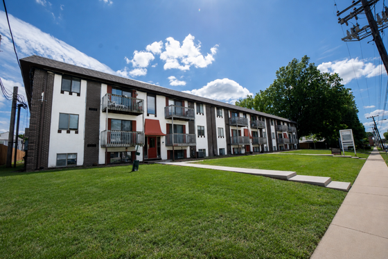 Charming mid-century style apartment building with balconies, surrounded by lush green lawn and vibrant blue sky.
