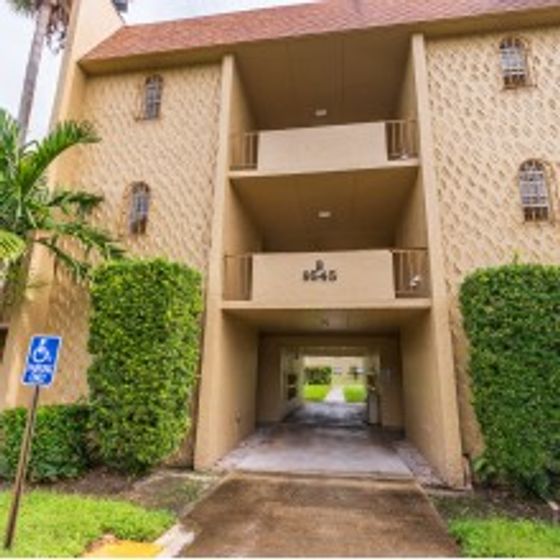 Green Briar West Apartments, exterior, tan 3 story building, entrance, bushes, grass, tree, handicapped parking sign
