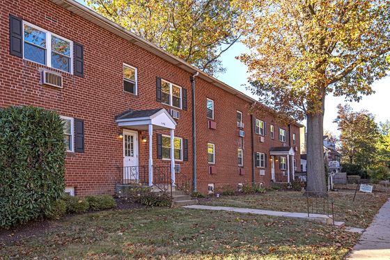 Quaint row of red brick townhouses with lush landscaping and mature trees in a peaceful neighborhood.