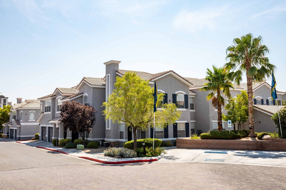 Modern apartment complex with lush landscaping, palm trees, and a sunny sky.