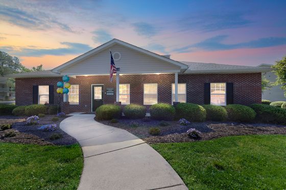 Charming brick building with inviting walkway, lush landscaping, and vibrant sunset in the background.