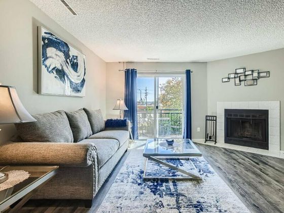 Elegant living room with modern decor, featuring a cozy sofa, stylish artwork, glass coffee table, and a fireplace, complemented by a view through large sliding doors.