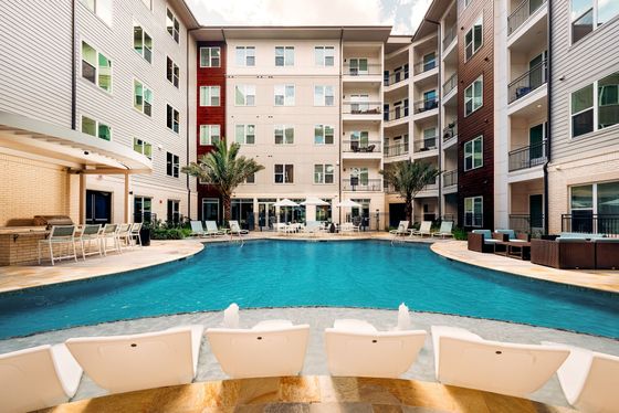 Luxurious apartment complex featuring a stunning outdoor pool, stylish lounge chairs, palm trees, and modern balconies creating a resort-style oasis.
