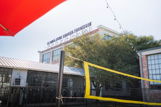 View of a stylish urban loft with a volleyball court in front, showcasing industrial charm and outdoor activity spaces.