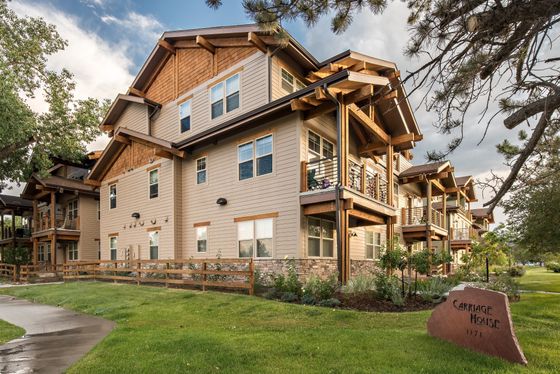 Elegant apartment building with wooden accents and balconies, surrounded by lush greenery.
