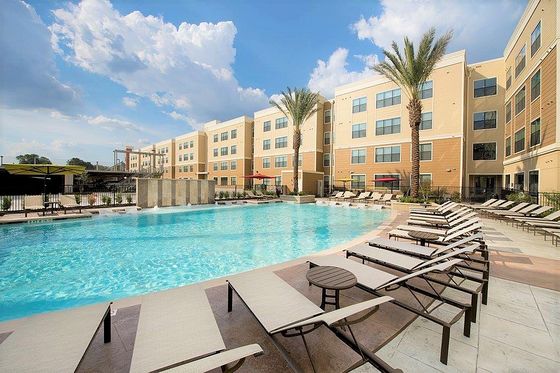 Elegant outdoor pool area surrounded by modern apartment buildings and palm trees under a clear blue sky.