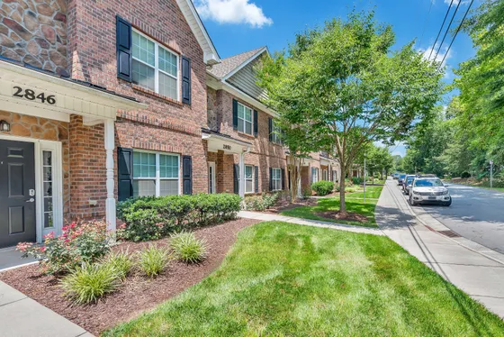 Charming brick townhouse exterior with manicured landscaping and a sunny walkway.