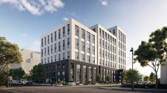Modern urban apartment building with sleek design, large windows, and lush landscaping under a clear blue sky.