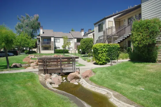 Twin Creeks apartment community exterior with landscaped courtyard, wooden footbridge over a creek, and two-story buildings