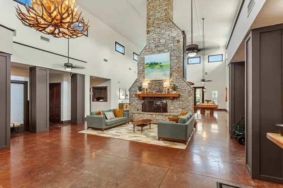 Inviting open-concept living room with a stunning stone fireplace, elegant antler chandelier, and cozy seating area on polished wood flooring.
