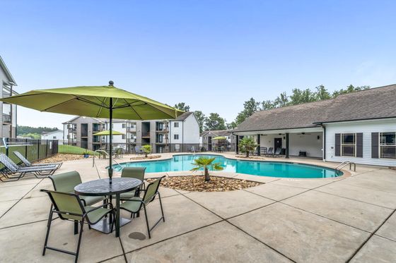 Inviting apartment complex pool area with lounge chairs, green umbrellas, and modern surroundings for relaxation and enjoyment.