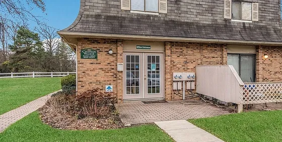 Charming brick-front office entrance in a picturesque residential complex, surrounded by lush greenery and neatly manicured lawns.