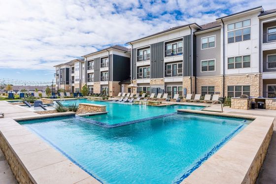 Luxurious apartment complex showcasing a sparkling outdoor pool with stylish lounge chairs and modern architecture.