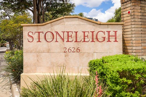 Inviting entrance to Stoneleigh apartments, featuring a stylish stone sign surrounded by lush greenery and vibrant flowers.