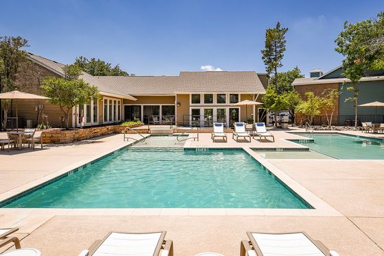 Luxurious apartment complex featuring a stunning pool, sun loungers, and vibrant gardens under a clear blue sky.